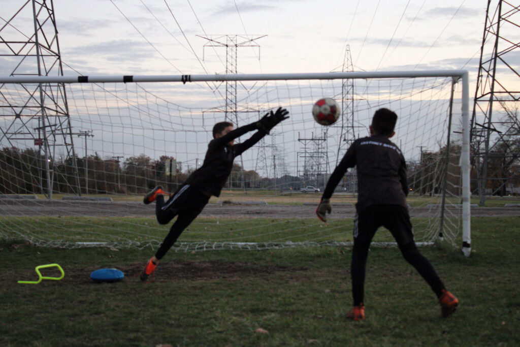 Goalkeeper diving to the top corner to save a high shot during Instinct Save Academy training
